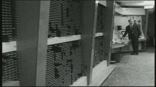 Black-and-white photograph of the TX-2 memory-bank hardware at MIT Lincoln Laboratory: rows of cabinet frames, wiring bundles, and indicator hardware typical of late-1950s machines. The image grounds the historical discussion of early partitioned arithmetic in real physical equipment.