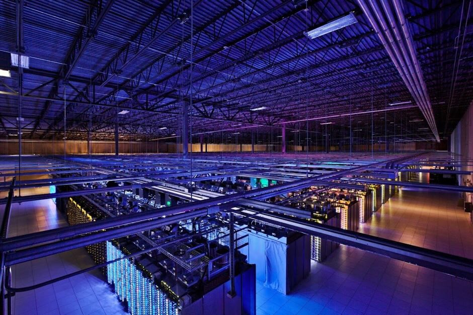 Wide interior photograph of a Google data center aisle with rows of server racks, cable trays, and overhead lighting in Council Bluffs, Iowa.
