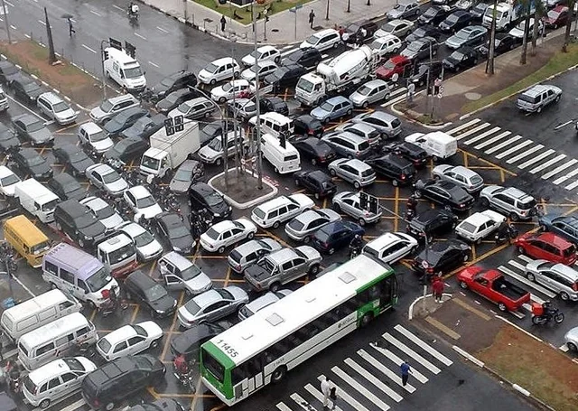 Photograph or stylized aerial diagram of vehicles gridlocked at an intersection, each lane waiting on another in a cycle so no car can proceed—mirroring circular wait in locking. Caption ties the visual metaphor to threads holding locks while waiting on peers.